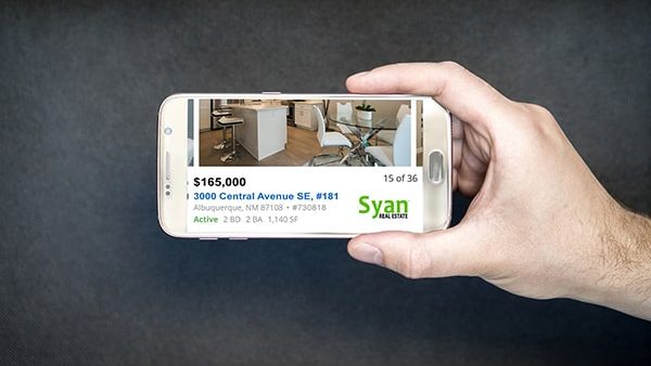 Hand holding phone with home listing on screen